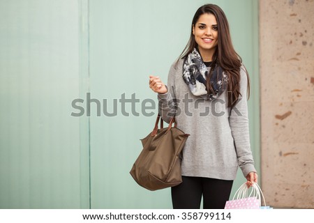 Pretty young woman carrying a purse and some shopping bags while visiting a shopping center