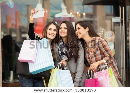 Group of cute female friends doing some shopping at a mall and taking a selfie with a smartphone