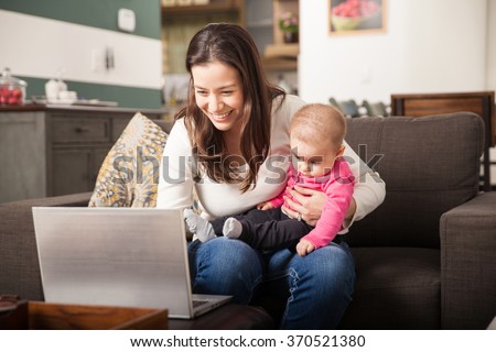 Cute young woman using a laptop computer for work at home while looking after her baby girl