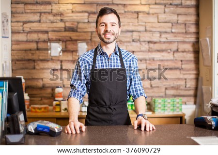 Portrait of a handsome young Hispanic business owner standing at the checkout counter and smiling