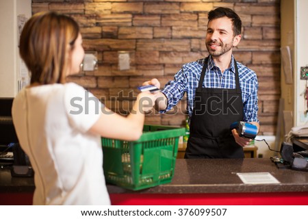 Handsome young man with a beard taking a credit card from a customer at a grocery store