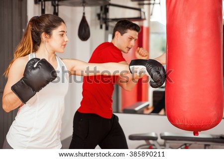 Good looking young woman with boxing gloves practicing on a punching bag next to her instructor
