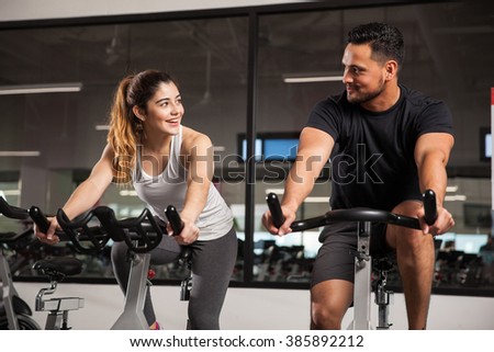 Beautiful young Hispanic woman flirting and talking to a guy while they both do some spinning at a gym. Focus on woman
