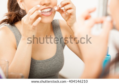 Closeup of a cute brunette applying a whitening strip on her teeth in front of a mirror in the bathroom