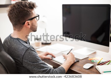 Rear view of a graphic designer using a pen tablet in front of a computer in an office. Blank computer screen