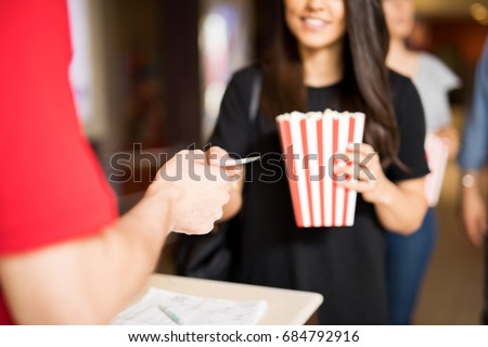Closeup of a woman holding a bag of popcorn and handing her ticket at the movie theater entrance