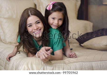 Portrait of young hispanic mother and her daughter having fun in the bedroom