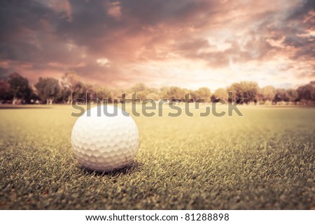 Golf ball lying on green field at sunset