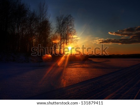 Beautiful frozen winter lake sunset with forest and clouds