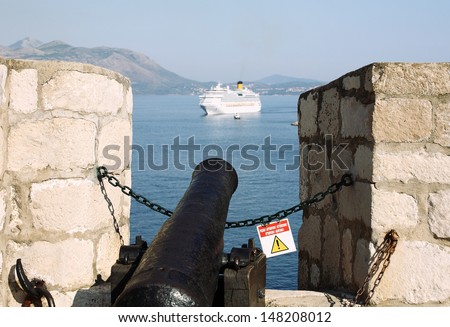 Tourism concept of an old cannon on a castle wall aiming at a cruise ship in the background
