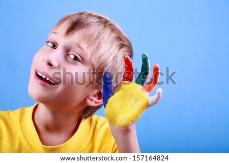 Beautiful cheerful blond boy in a yellow t-shirt showing a multicolored painted hand near his ear smiling happily