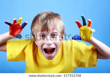 Beautiful cheerful blond boy in a yellow t-shirt showing multicolored painted hands and smiling happily