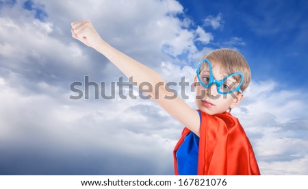 Cute little child dressed as super hero stretching his hand against blue sky