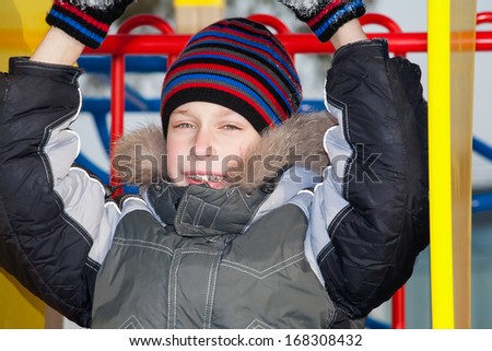 Beautiful happy boy wearing winter jacket and a hat playing on a playground smiling