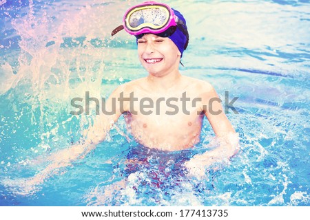 Child wearing a colorful swimming mask splashing water colors  in an open-air swimming pool