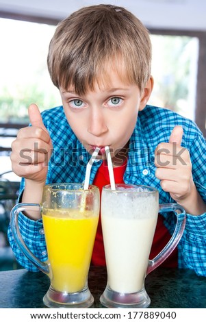 Cute funny child drinking fruit cocktails from two big glasses with straws. Creative drink concept.