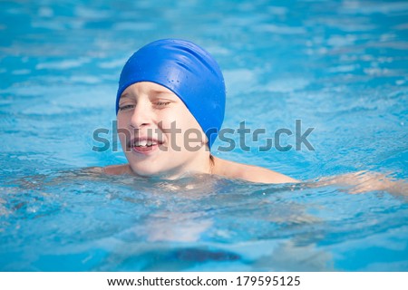 Cute funny child in a swimmer cap swimming in a sunny pool