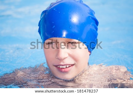 Cute funny child in a swimmer cap swimming in a sunny pool