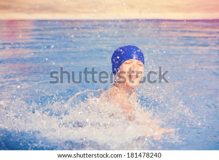 Child wearing a colorful swimming hat splashing water in an open-air swimming pool and laughing