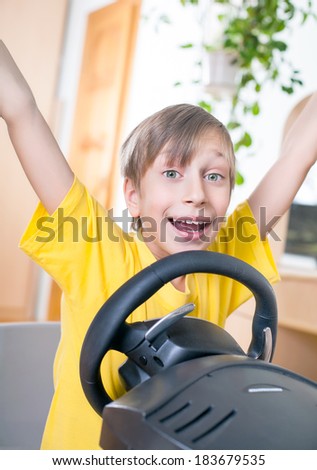 Funny child driver in a yellow t-shirt playing at a computer raising his hands in excitement