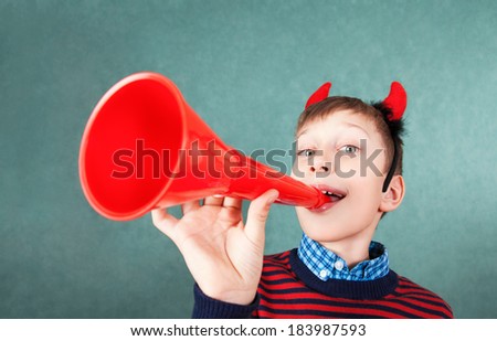 Funny schoolboy pretending to be the devil with horn playing red pipe smiling. Behavior concept