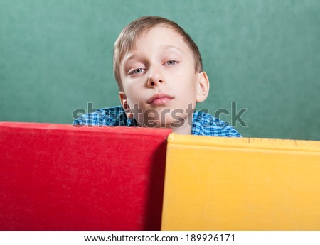 Cute funny little boy sitting in a classroom with colorful books looking bored
