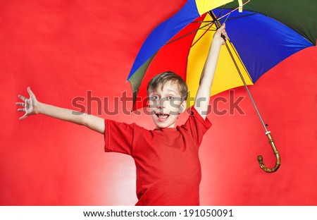 Beautiful funny boy boy in red t-shirt holding a multicolored umbrella standing over red background with funny expression