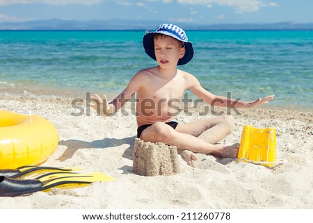 Funny little child with a panama sitting on beach with swimming accessories and relaxing