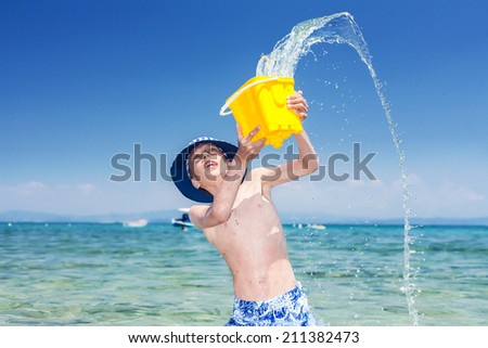 Funny little boy with a panama playing in the sea throwing a yellow toy bucket of water