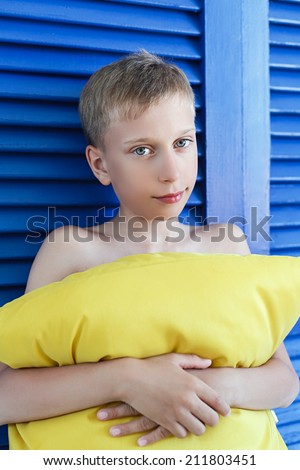 Candid portrait of a beautiful little child holding a pillow standing by a window with venetian blinds looking into camera smiling