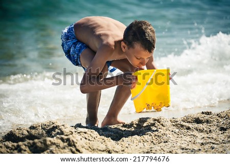 Funny little boy playing in sea with toy bucket. Summer break concept.