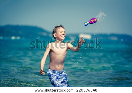 Cute cheerful child in swimware playing in sea with toy. Summer break concept.
