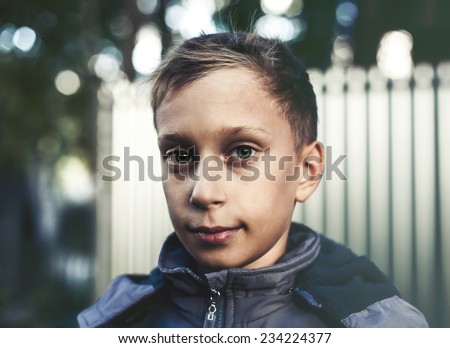 Funny sad little boy standing outdoors looking into camera. Adoption and donation concept.