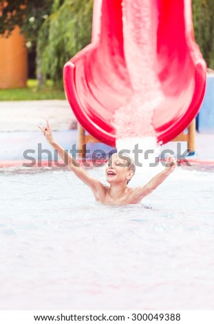 Funny cheerful child enjoying summer vacation in water park taking a ride in excitement.