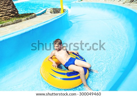 Funny child enjoying summer vacation in water park taking a ride on yellow float