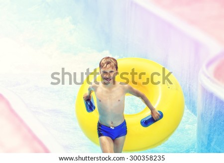 Funny excited child enjoying summer vacation in water park riding on slide with yellow float laughing.