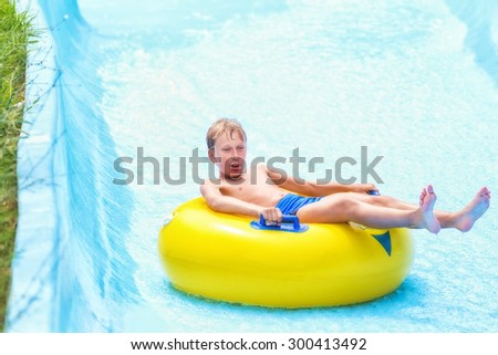 Funny excited child enjoying summer vacation in water park riding on slide with yellow float