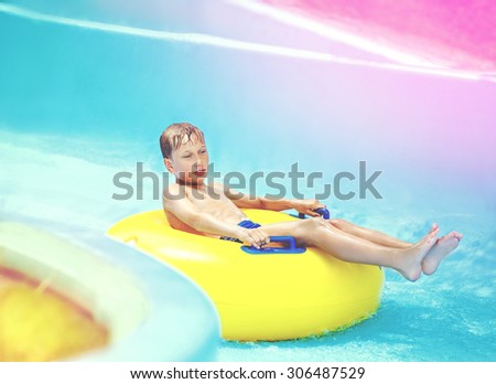 Cute child enjoying summer vacation in aqua park riding on yellow float