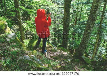 Man wearing red raincoat walking along a path in mountain forest taking photo