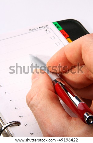 Hand with a red pen writing in an organizer on white