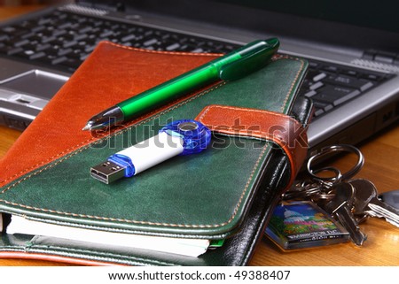 brown leather organizer, USB key and a green pen on a notebook