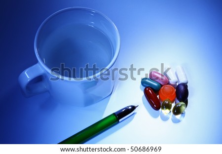 white cup, green pen and colourful pills (red, yellow, green) on blue