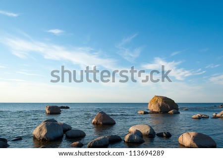 Low angle view of a rocky ocean coastal background with calm blue seas and light cloud in the sky