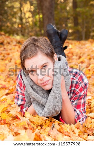 Attractive woman lying on her stomach in a bed of colorful yellow orange autumn leaves scattered on the ground marking the changing of the seasons