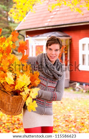 Attractive woman collecting autumn leaves for use in decorating the house carrying a wicker basket full of colorful orange yellow twigs covered in fall leaves