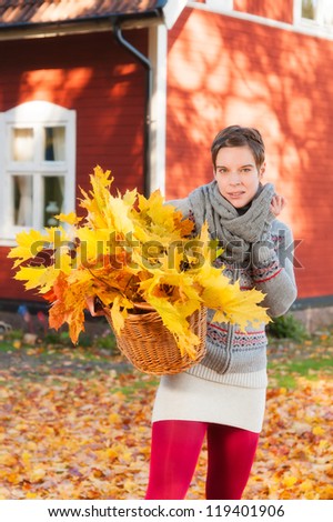 Attractive woman collecting autumn leaves in front of a typical red wooden house in Sweden