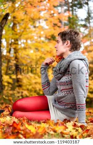 Young attractive woman, dressed in mini skirt, sitting in autumnal foliage enjoying the fall
