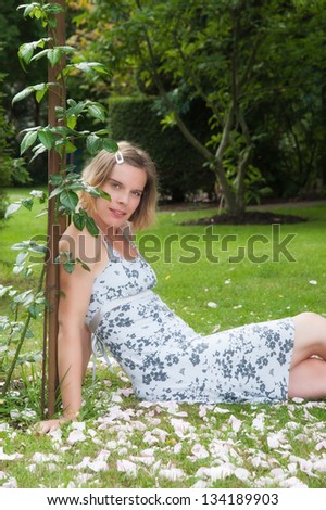 Attractive young woman sitting under a pergola with roses in a enchanting garden