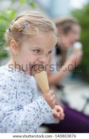 Very cute little girl with blonde hair eating chocolate ice cream and and is about to take a big bite