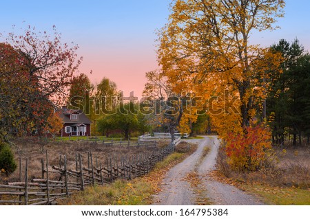 Landscape in the province of Smaland in the south east of Sweden. Typical view with dirt road and wooden fences and in the background a red wooden house